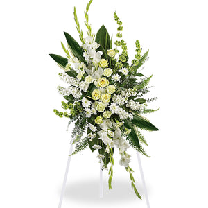 Standing sympathy spray arrangement featuring white lilies, white and yellow roses, snapdragons, carnations, and lush greenery displayed on an easel against a white background.