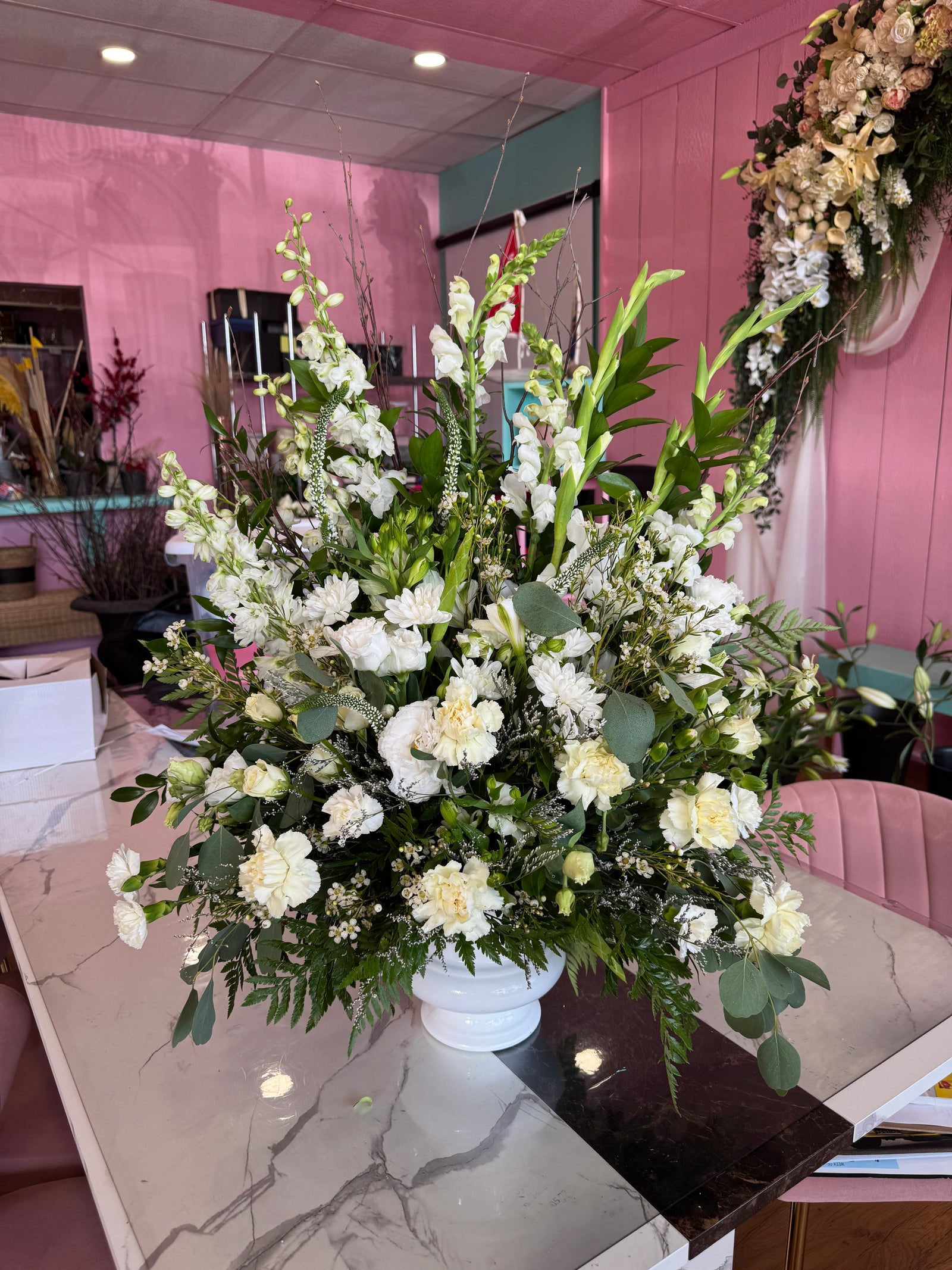 Standing sympathy spray arrangement featuring white lilies, white and yellow roses, snapdragons, carnations, and lush greenery displayed on an easel against a white background.